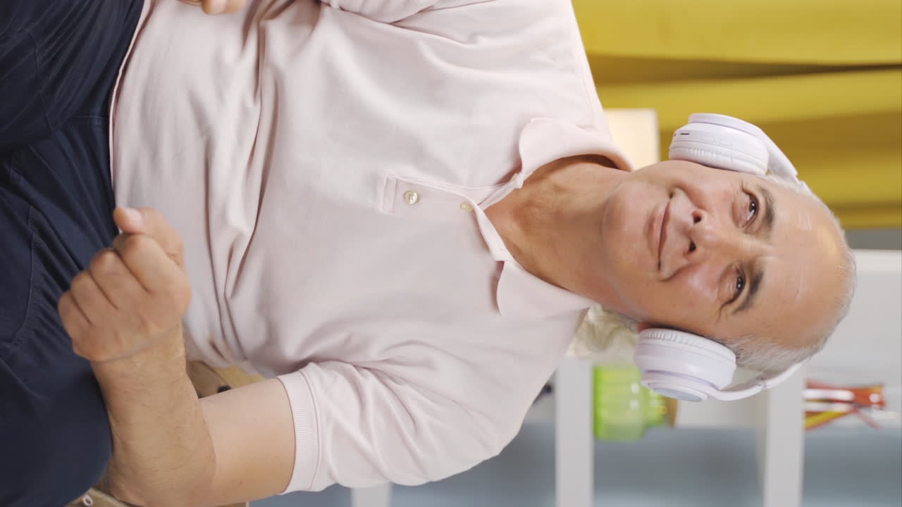 Vertikal video av gammel mann som ser ut av vinduet og lytter til musikk med hodetelefoner