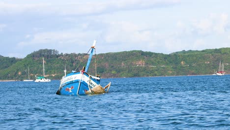 a fishing boat gradually sinks in the ocean near phuket, thailand, under clear skies with distant hills in the background