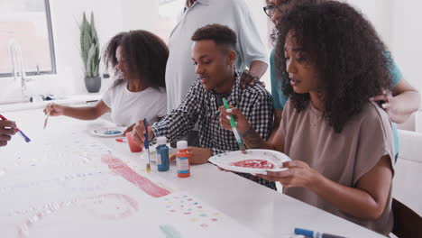 Three-young-black-adults-make-a-sign-for-a-surprise-party-with-their-family-in-the-kitchen,-close-up