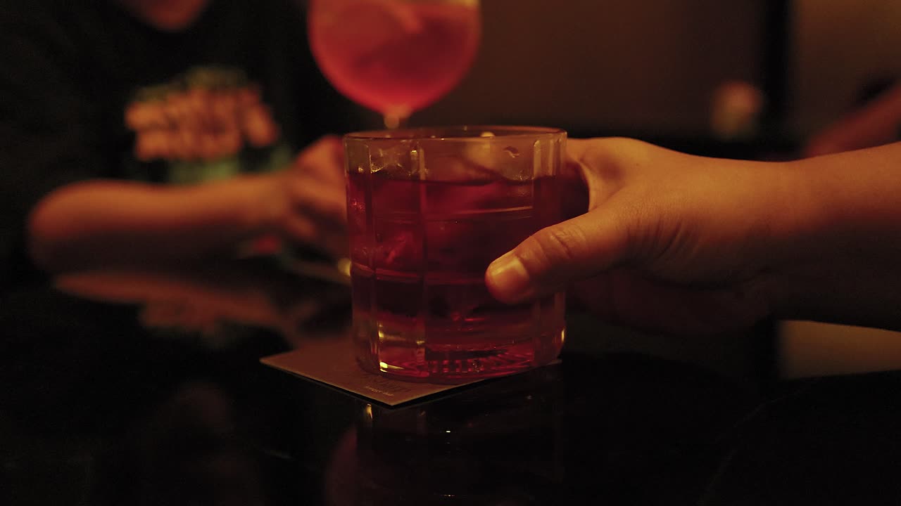 mani che si scambiano un cocktail in una scarsa illuminazione