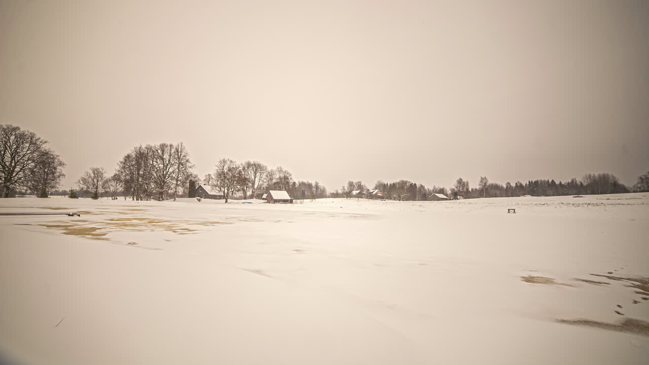 Timelapse di neve che copre il suolo sciogliendosi lentamente lungo la campagna con la vista di una casetta di paese sullo sfondo.