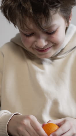 smiling caucasian kid peeling the tangerine. healthy lifestyle, child consuming fruit at home. close up. vertical video