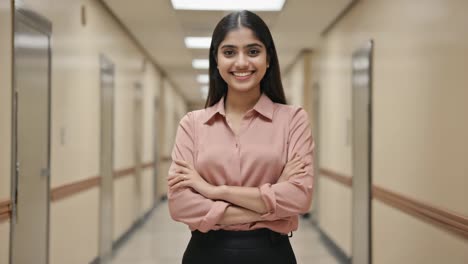 professional indian businesswoman standing confidently, arms crossed, within sleek corporate hallway, reflecting corporate success and leadership
