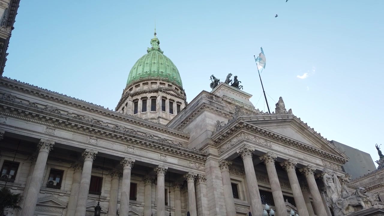 Plano de establecimiento en contrapicado del Palacio del Congreso Nacional, la Bandera Argentina y pájaros volando en Buenos Aires