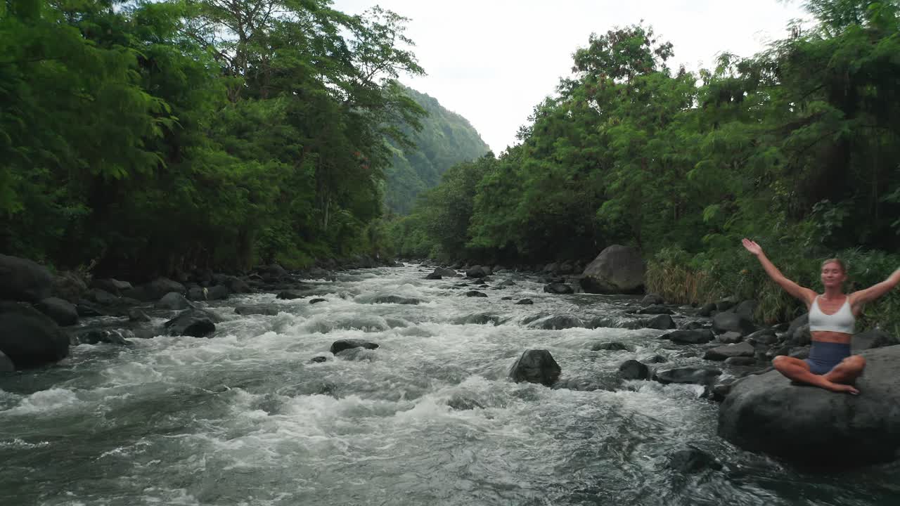 Concetto "un tutt'uno con la natura", donna che medita in posizione del loto su una roccia, con il fiume che scorre