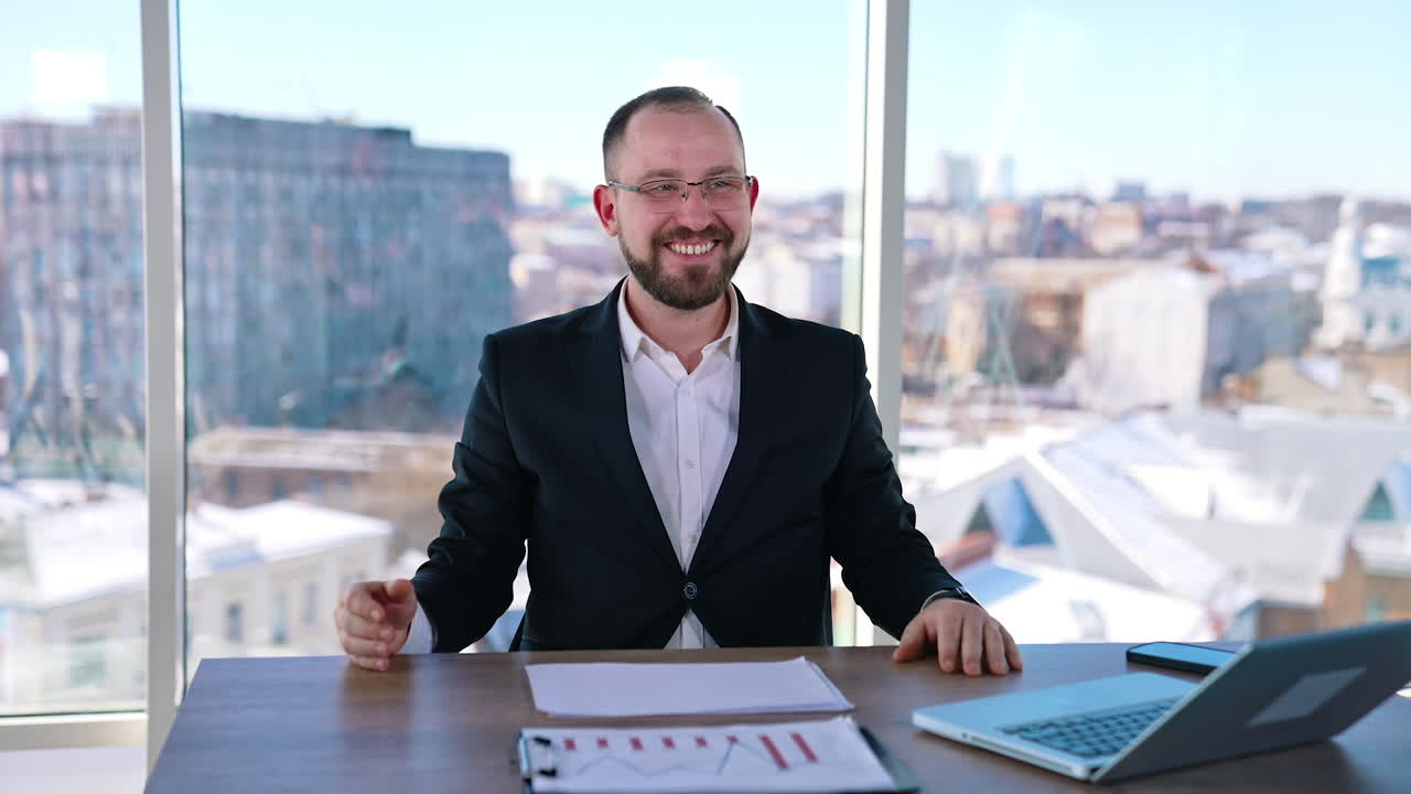 Astonished businessman at workplace. Smiling office worker sitting at the table with a laptop on window background with city view.