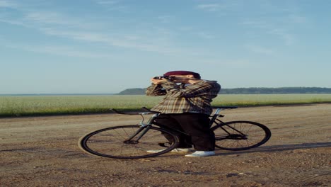 man taking pictures with a vintage camera on a bike in a field