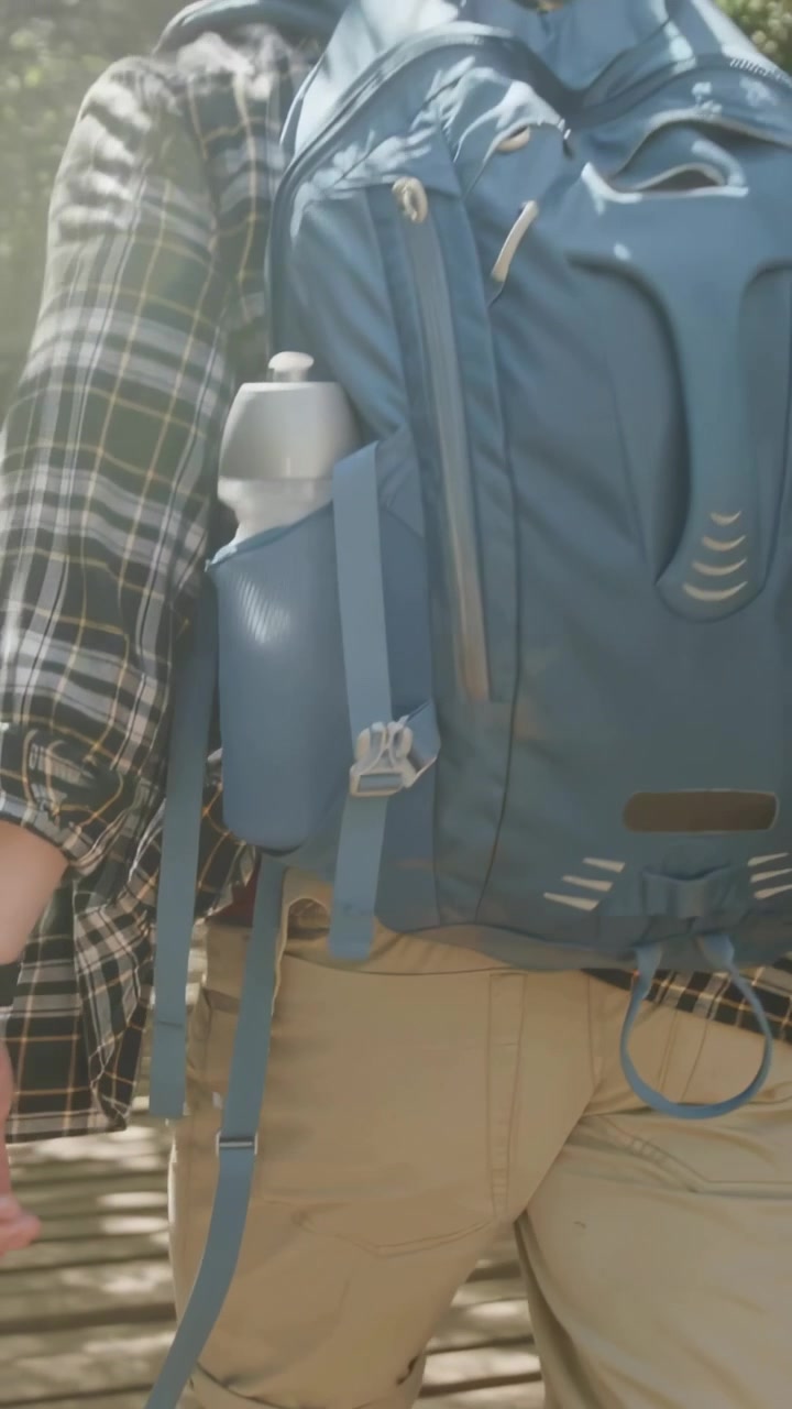 Video verticale: Escursionista che cammina con camicia a quadri annodata, zaino blu su una passerella, la luce del sole che invita all'escursione.