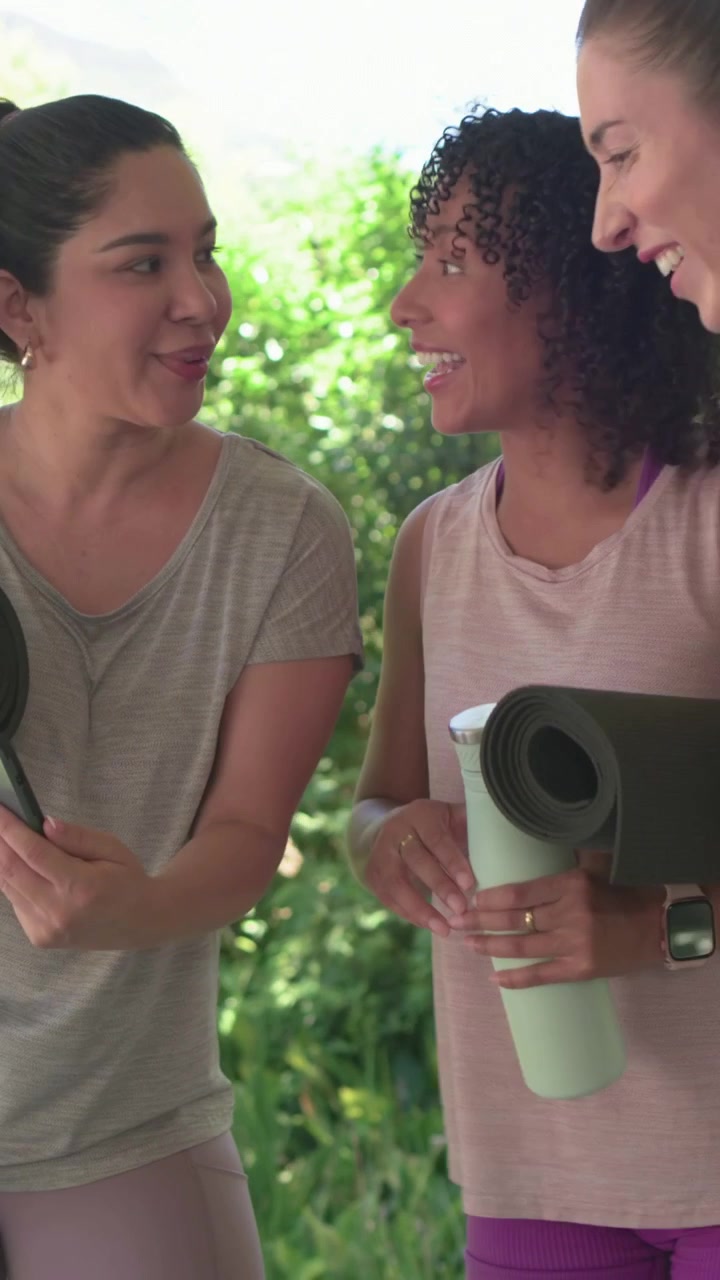 Video verticale: Donne che arrivano in abbigliamento da palestra, si salutano, guardano il telefono sul patio e tengono i tappetini per lo yoga.