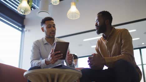 video di due uomini d'affari diversi che parlano e usano il tablet nell'area lounge di un ufficio affollato