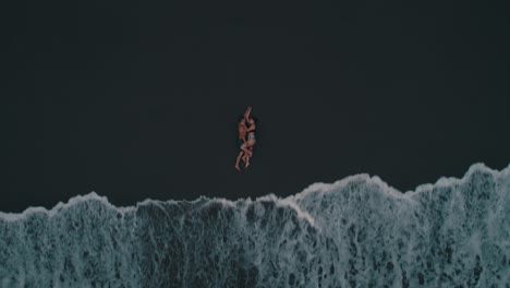 top view of romantic couple lying down on the black beach
