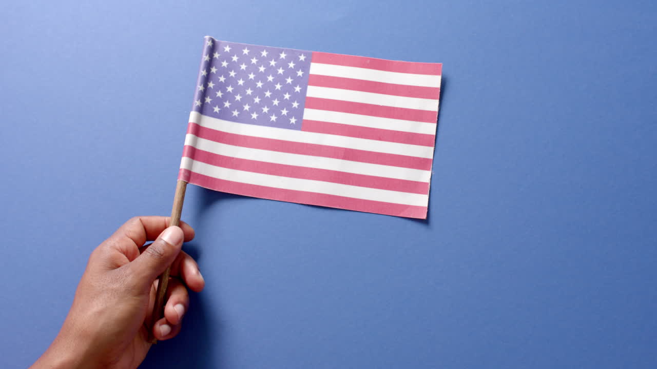 Primo piano di mano che tiene la bandiera nazionale degli Stati Uniti d'America su sfondo blu