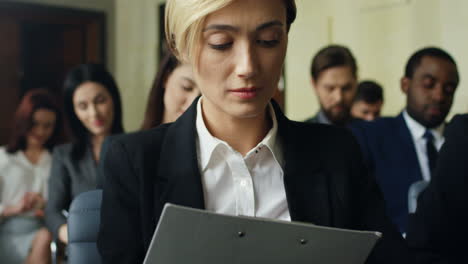 close-up view of caucasian businesswoman sitting among the audience in a conference room and writing on a document while listening