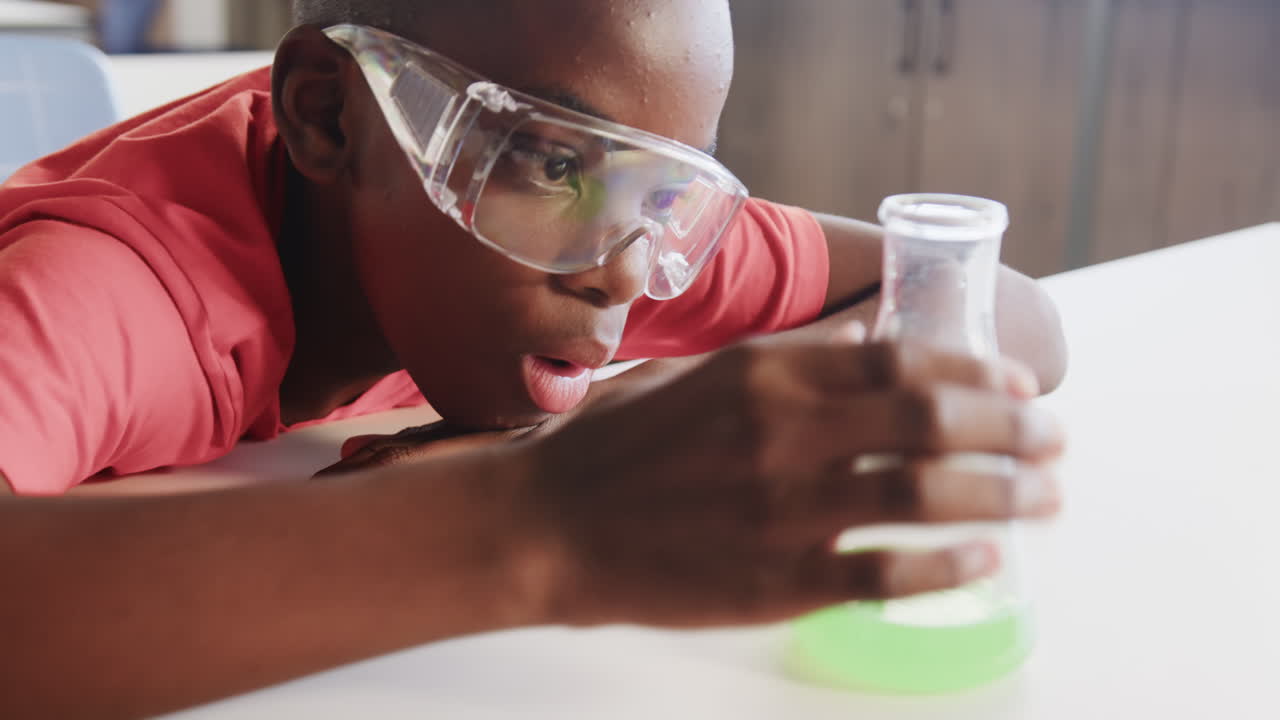 In school, boy wearing safety goggles observing green liquid in beaker