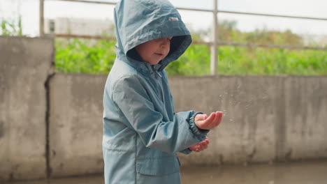 el niño coloca la mano debajo de las gotas de lluvia que caen el niño pequeño hizo una mueca debido a las salpicaduras en la cara