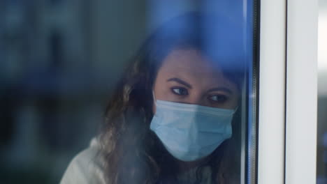 mujer mirando por una ventana mientras lleva una máscara