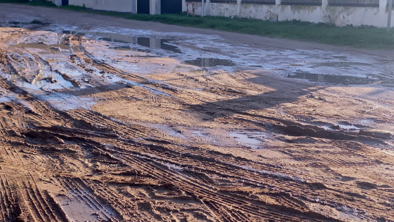 Le tracce di fango e le pozzanghere riflettono la tenue luce del mattino su una strada di accesso costiera sabbiosa dopo la pioggia