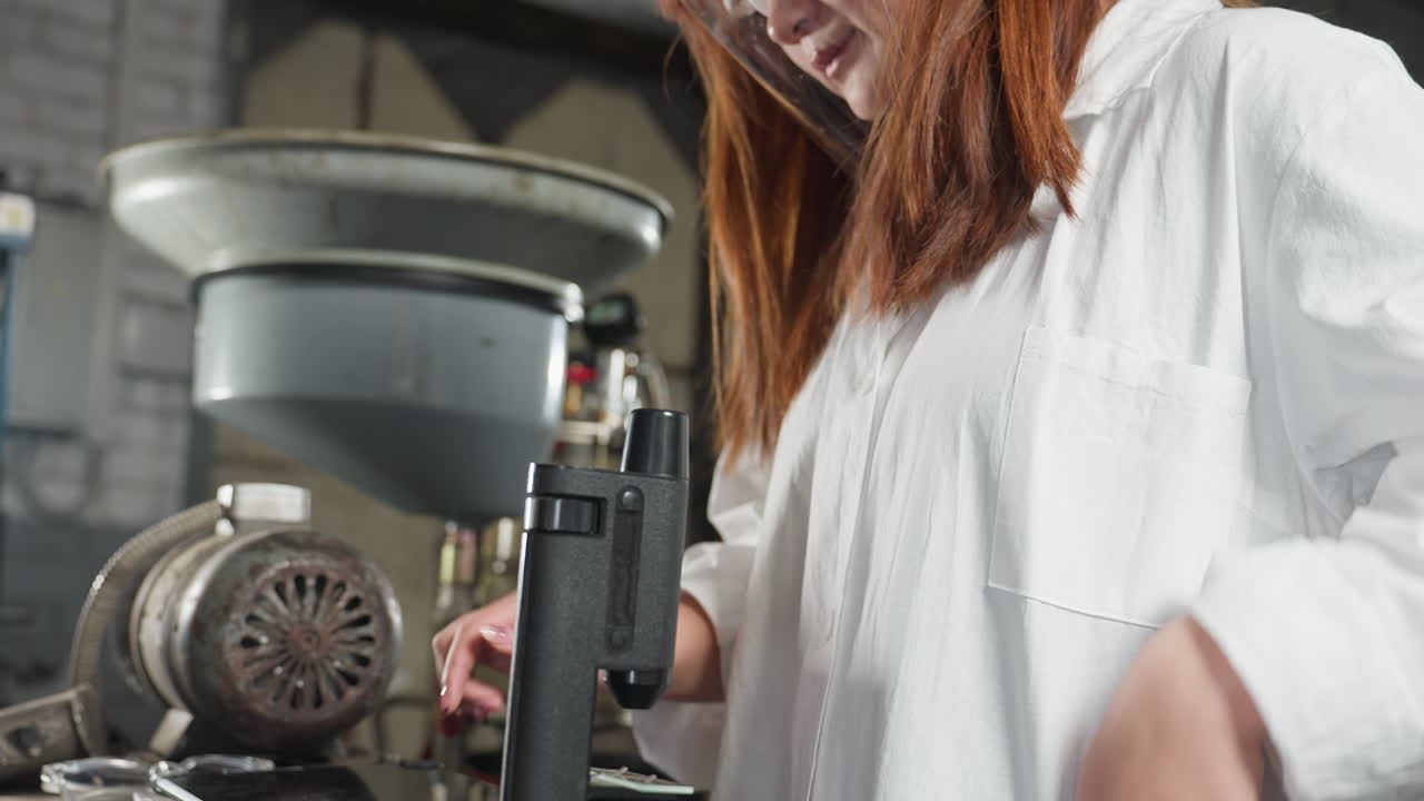 학생은 현미경을 통해 관찰하기 위해 구부러지면서 머리카락을 조정합니다. 머리카락은 어깨를 가로질러 아져 나옵니다. 그리고는 자동차 작업실에서 도구, 기계 및 밝은 빛을 특징으로하는 태블릿을 누르기 위해 곧게됩니다.