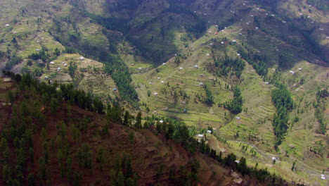 Vista-Aérea-Sobre-La-Cima-Del-Bosque-De-Montaña-Y-El-Valle-Hasta-Las-Montañas-Heladas,-Las-Nubes-Están-Tocando-La-Cima-De-Las-Montañas-Heladas,-Cerca-De-La-Cima-De-La-Colina