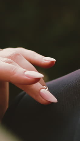 cu, slow motion: graceful young bride hand with wedding ring strokes shoulder of man wearing black suit with tie bow extreme close view
