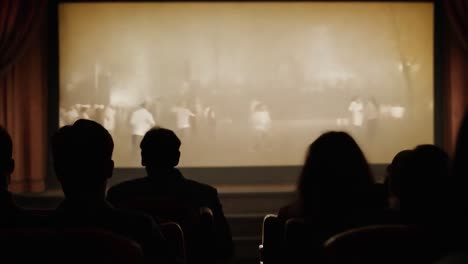 silhouettes of an audience sitting in a dark theater, captivated by the film projected on the screen