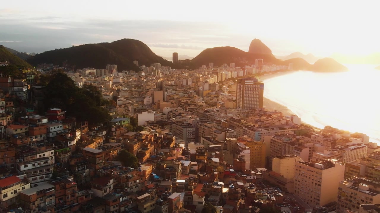 Un drone si allontana sopra una favela di Rio rivelando la spiaggia di Copacabana al tramonto dorato