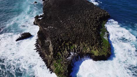 aerial view of powerful ocean waves crashing against a rugged rocky coastline