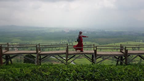 Fröhliche-Junge-Frau-In-Muslimischem-Kleid,-Die-Auf-Einer-Holzbrücke-Mit-Wunderschönem-Blick-Auf-Die-Natur-In-Den-Teeplantagen-Spazieren-Geht