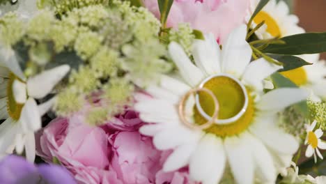 two golden shining wedding rings isolated on a white flower bouquet - wedding ring background concept