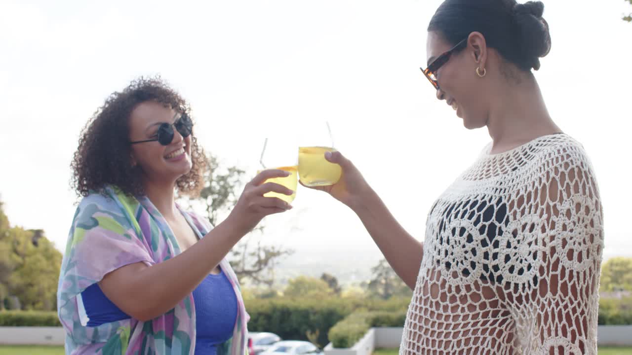African American friends toasting glasses, chatting on terrace in crochet coverups