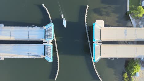 aerial view of boats, including a sail boat, passing through an open drawbridge