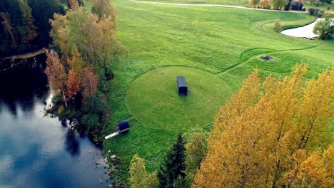 aerial shot of grass field with barrel sauna next to natural lake during daytime