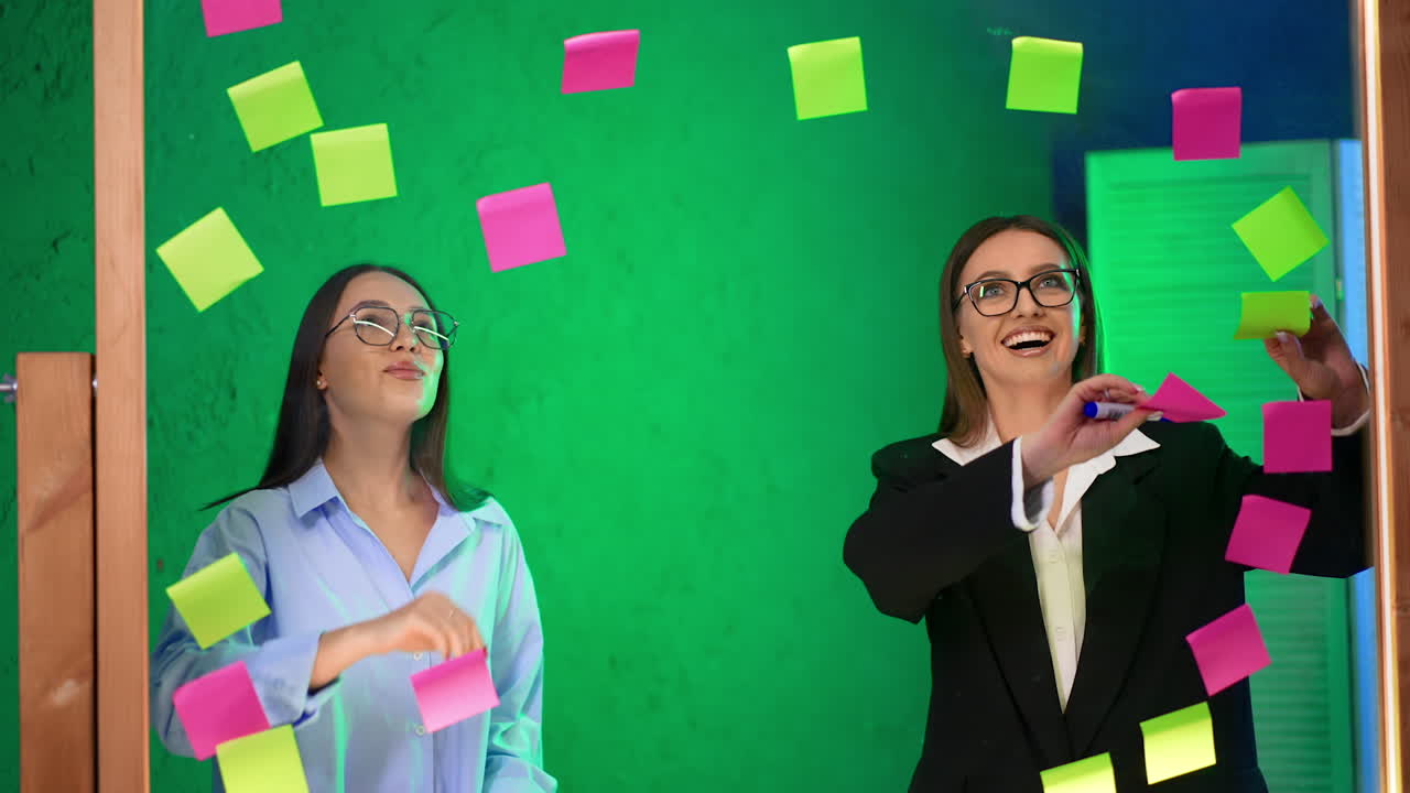 Cheerful ladies in the office take away stickers from the glass board. Business, startup, planning, management and people concept.