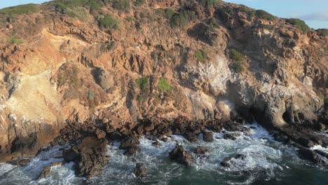 Drone pulls back and tilts up over ocean cliffs in Malibu (60fps)