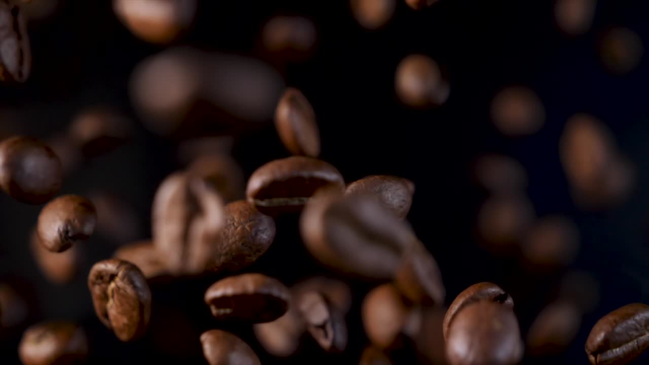 granos de café tostados en cámara lenta. granos de cafe en caída libre. flotando en el aire sobre un fondo oscuro. 4k en imágenes en bucle.
