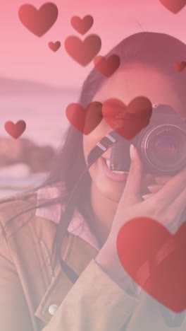 animation of hearts floating over happy biracial woman taking photo at cabriolet