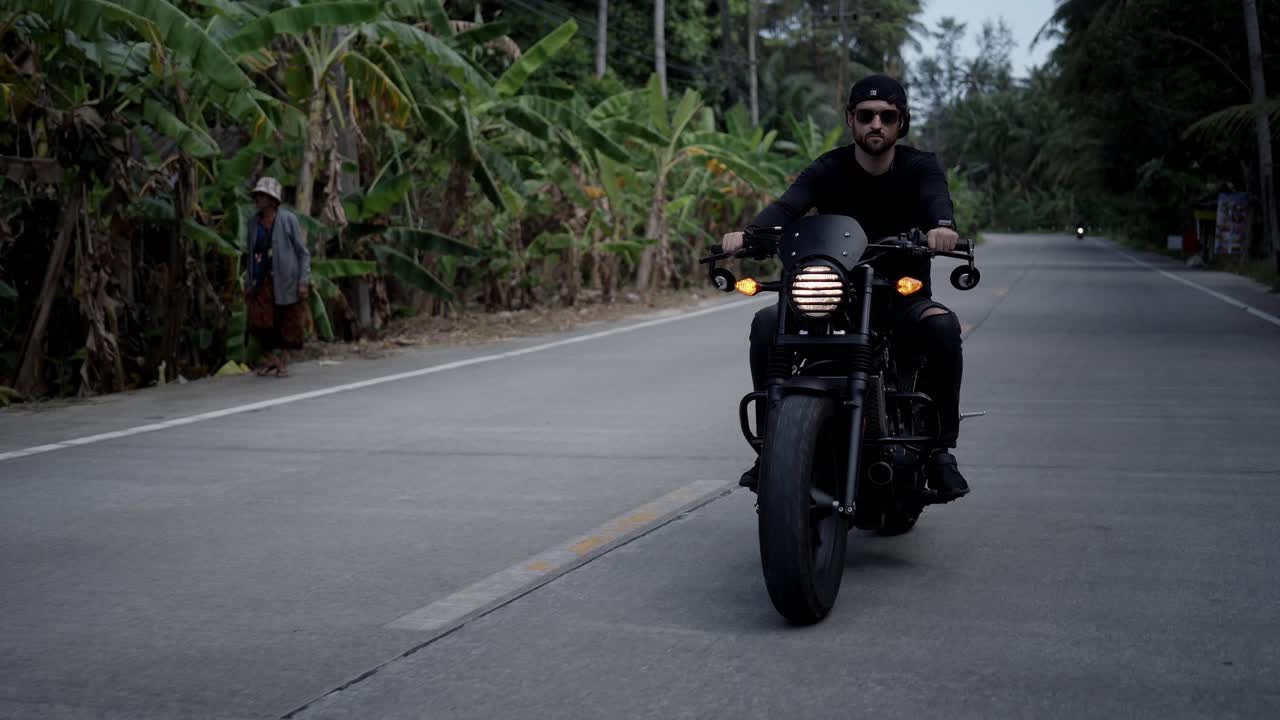 Uomo che guida una moto nera su una strada tropicale