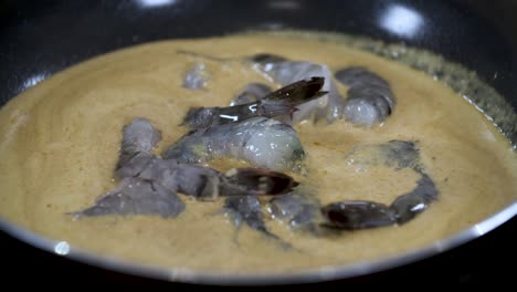 adding raw fresh blue grey colored shrimps into asian yellow coconut cream curry