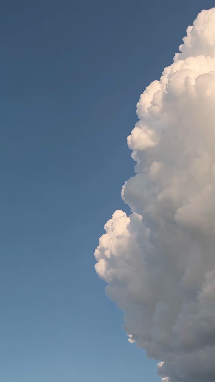 Vertical video capturing a low-angle view of a towering cumulus cloud against a clear blue sky
