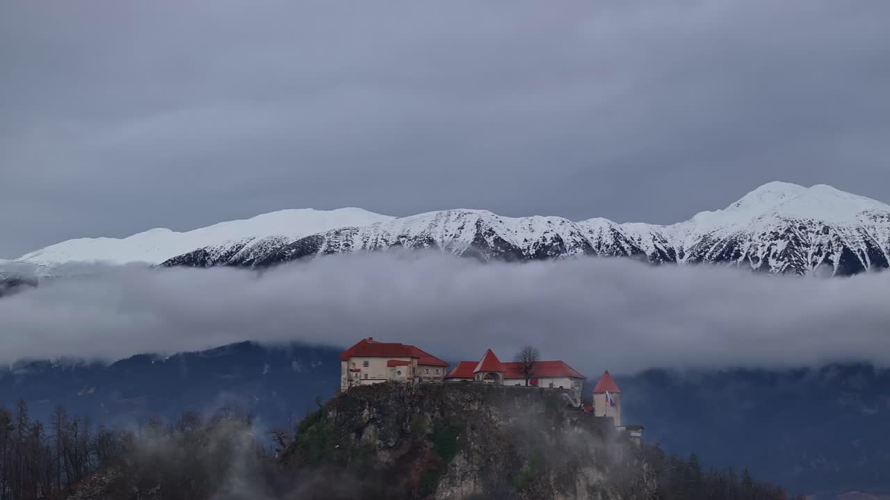 Una ripresa con drone focalizzata sul castello di Bles, con le nuvole basse e le montagne innevate sullo sfondo