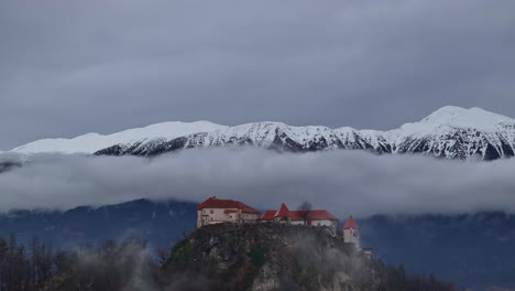 a drone shot focused in the bles castle, with the low clouds and the snowy mountains in the background