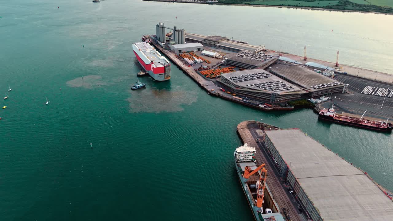 Mid-angle aerial drone pans left above Southampton port docks, capturing cargo ships, containers, and sea waters glowing under warm autumn sunset light across the busy maritime hub