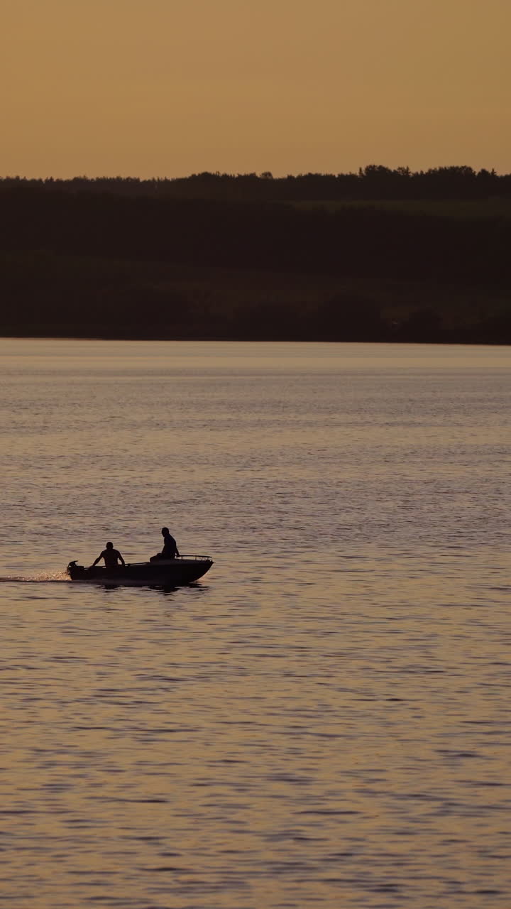 Motor boat floating in water on the forest background at dusk. Two people in a boat swimming along the river in the evening. Vertical video