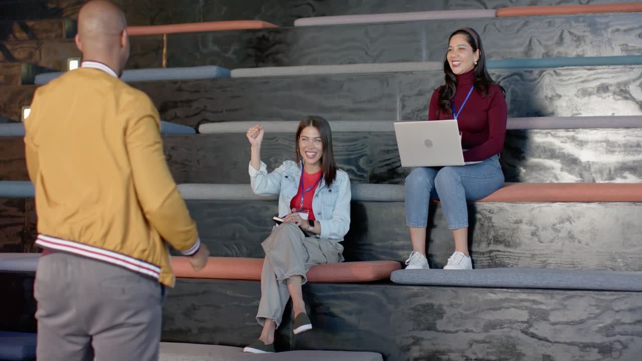 Compañeros de trabajo diversos en un anfiteatro de oficina, un presentador haciendo una pregunta y voluntarios escribiendo en laptops.