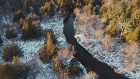 Sobrevuelo-Aéreo-Del-Río-En-Un-Paisaje-Forestal-Invernal,-árboles-Iluminados-Al-Atardecer