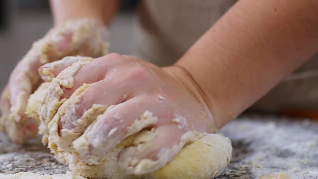 Primo piano al rallentatore di una mano che impasta la pasta, enfatizzando la morbida consistenza e il movimento mentre l'impasto viene lavorato a mano in cucina