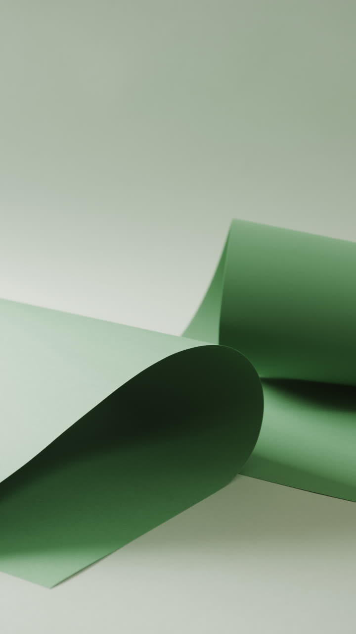 Vertical video of close up of green rolled pieces of paper on pale green background with copy space