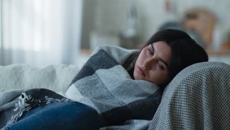 woman sitting on a sofa, wrapped in a blanket, looking unhappy