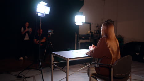 rear view of a brunette long-haired woman recording a video in studio. male cameraman and female assistant work backstage.