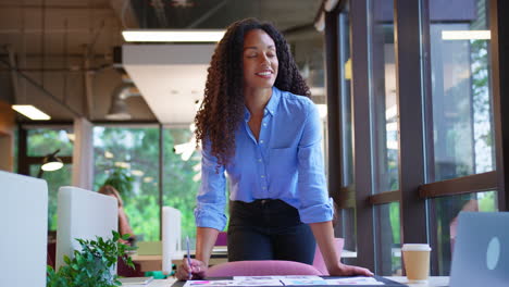 businesswoman standing at desk in office approving or checking proofs or design layouts